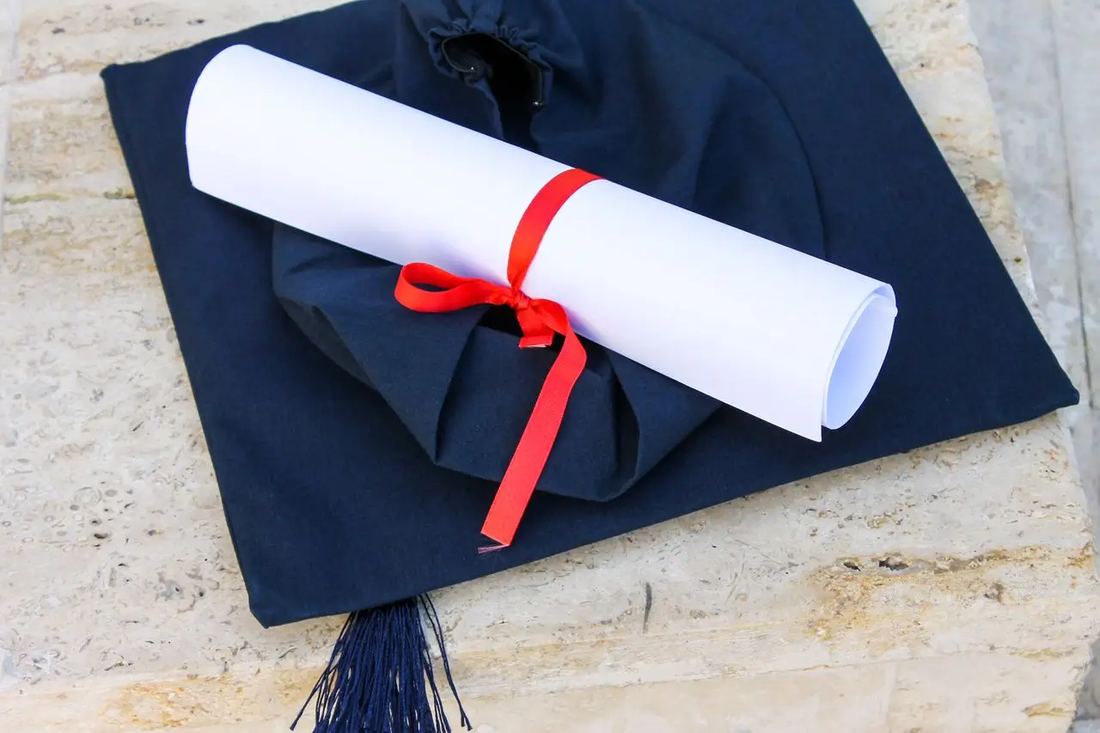 A graduation cap and a rolled diploma tied with a red ribbon